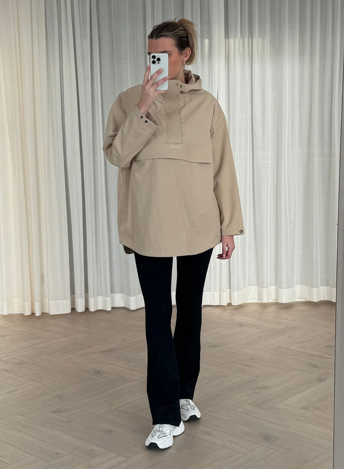 Nainen yllään aim'n Beige Waterproof Oversized Anorak, mustat leggingsit ja valkoiset lenkkarit ottamassa peiliselfietä.