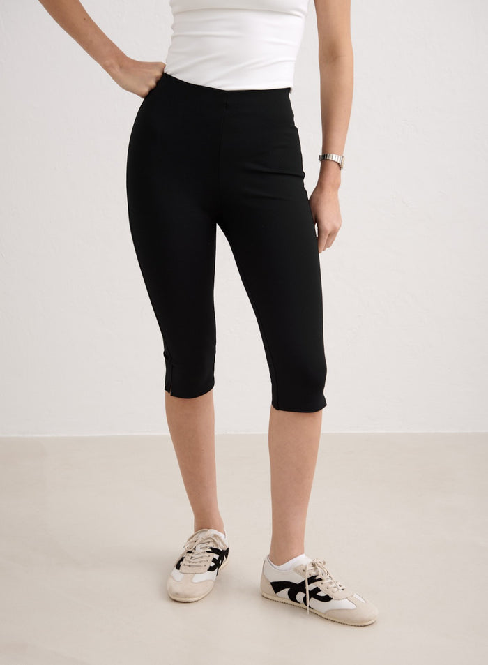 Tyylikkäät mustat aim'n Luxe Capri Pants -housut 3/4-pituudella, stailattuna valkoisilla tennareilla. [34-174cm]