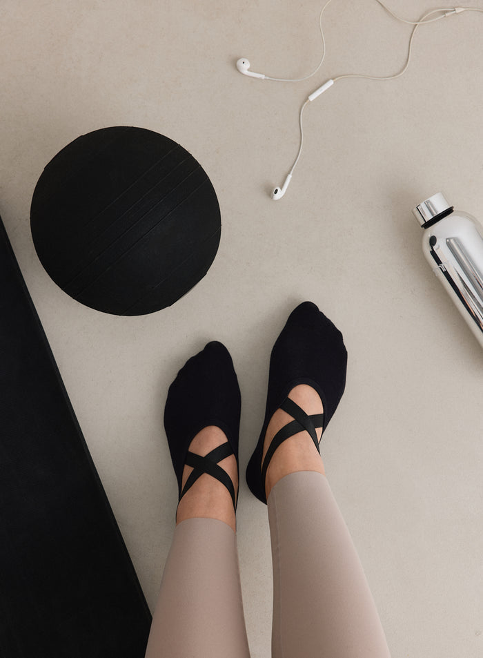 Ylhäältä päin kuvattu näkymä henkilöstä, jolla on yllään mustat aim'n Pilates Socks -sukat.