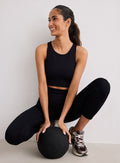 Hymyilevä nainen yllään musta Ribbed Seamless Crop Top ja yhteensopivat leggingsit, kyykistyneenä kuntopalloa pidellen [XS-170cm]