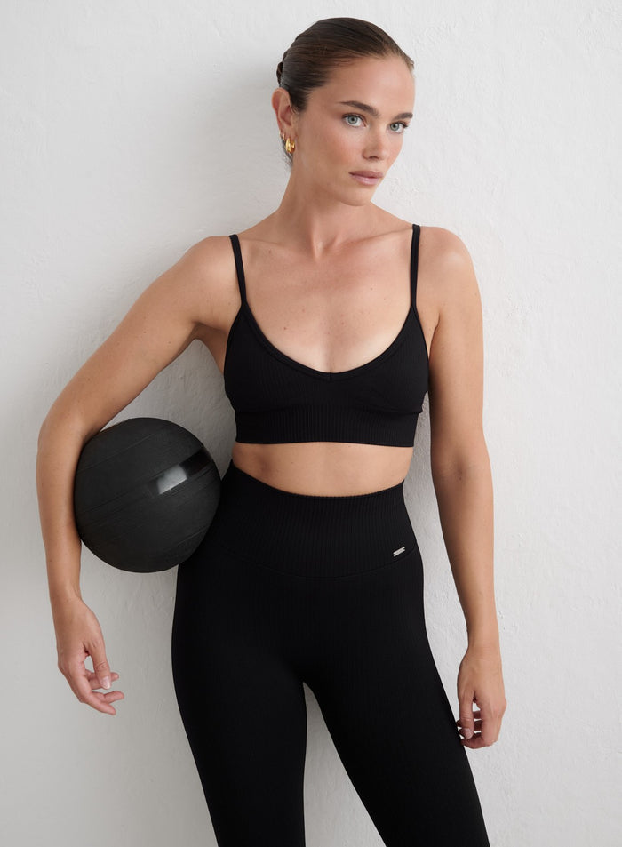 Mustat aim'n Ribbed Seamless Deep Cut Bra -liivit ja leggingsit kuntopalloa pitelevän mallin yllä. [S-165cm]