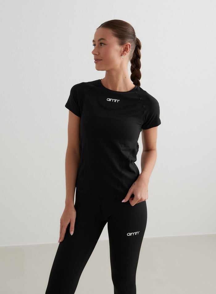 Musta lyhythihainen aim'n Soft Basic -treenitoppi valkoisella logolla ja yhteensopivat mustat leggingsit.