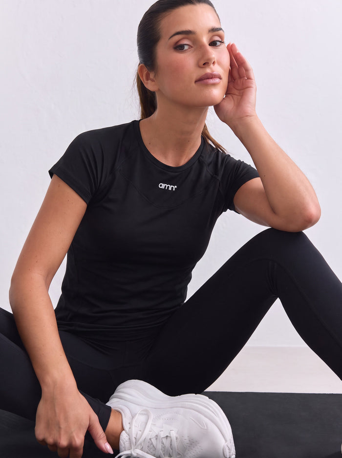 Musta aim'n Soft Basic Short Sleeve -toppi raglan-hihoilla ja valkoisella logolla pääntiellä.