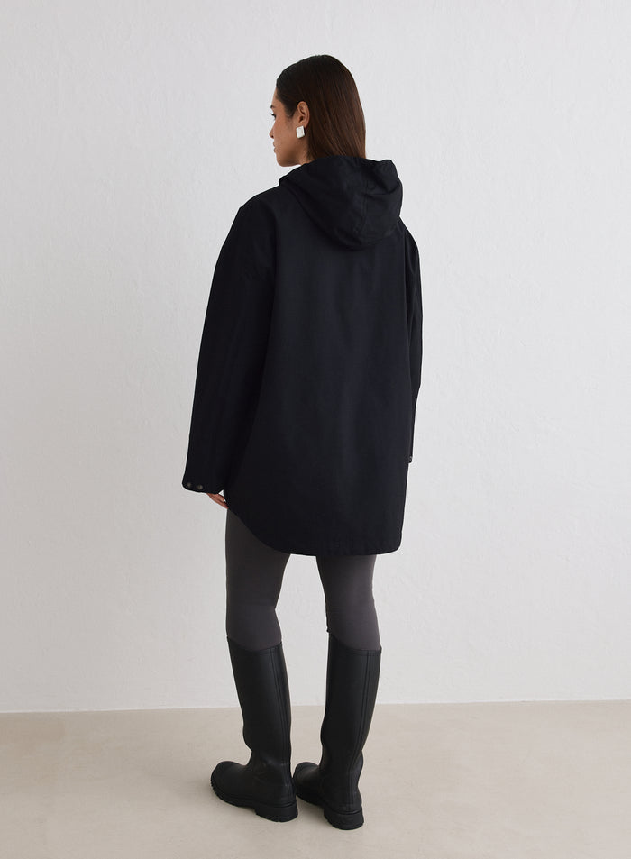 Nainen takaapäin yllään musta Waterproof Oversized Anorak, tummat leggingsit ja mustat saappaat [M-174cm]
