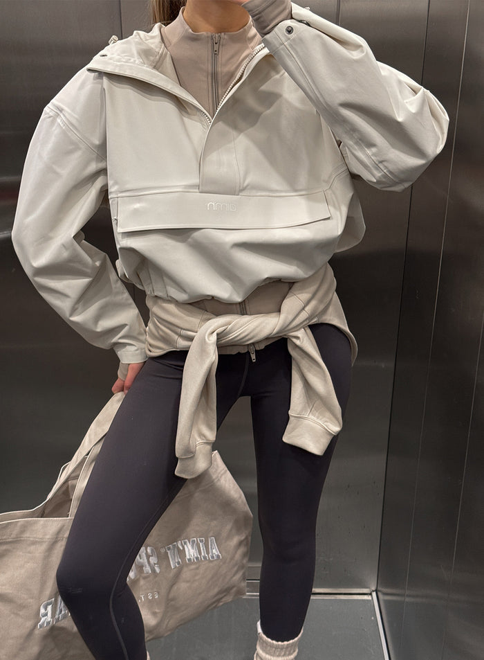 Clay-värinen lyhyt vedenpitävä aim'n-anorakki, tummat leggingsit ja vyötärölle solmittu collegepaita.