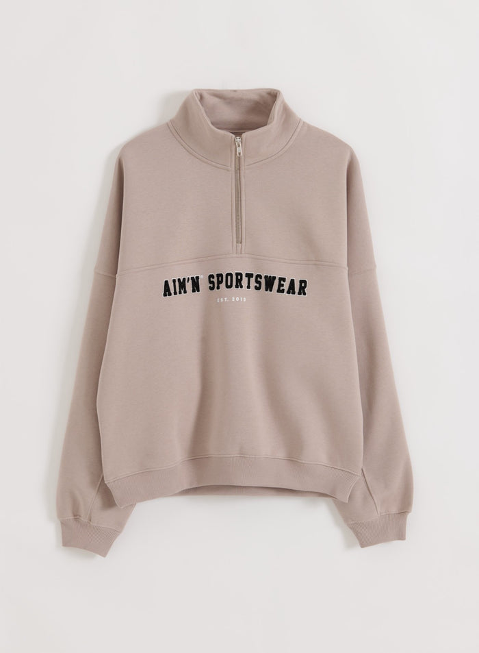 Pehmeä Dark Clay -sävyn Varsity Sweat Half Zip pystykauluksella ja aim'n-kirjailulla rinnassa.