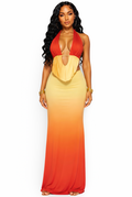 A woman modeling a halter-neck maxi dress with a gradient color-blocked design transitioning from red at the top, through orange, to yellow at the bottom, against a plain white background.