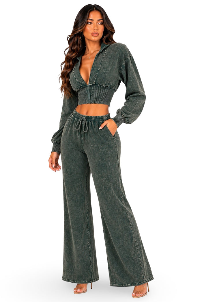 A woman modeling a matching two-piece outfit consisting of a dark green acid-wash long-sleeve crop top and matching wide-leg drawstring pants, set against a plain white background.