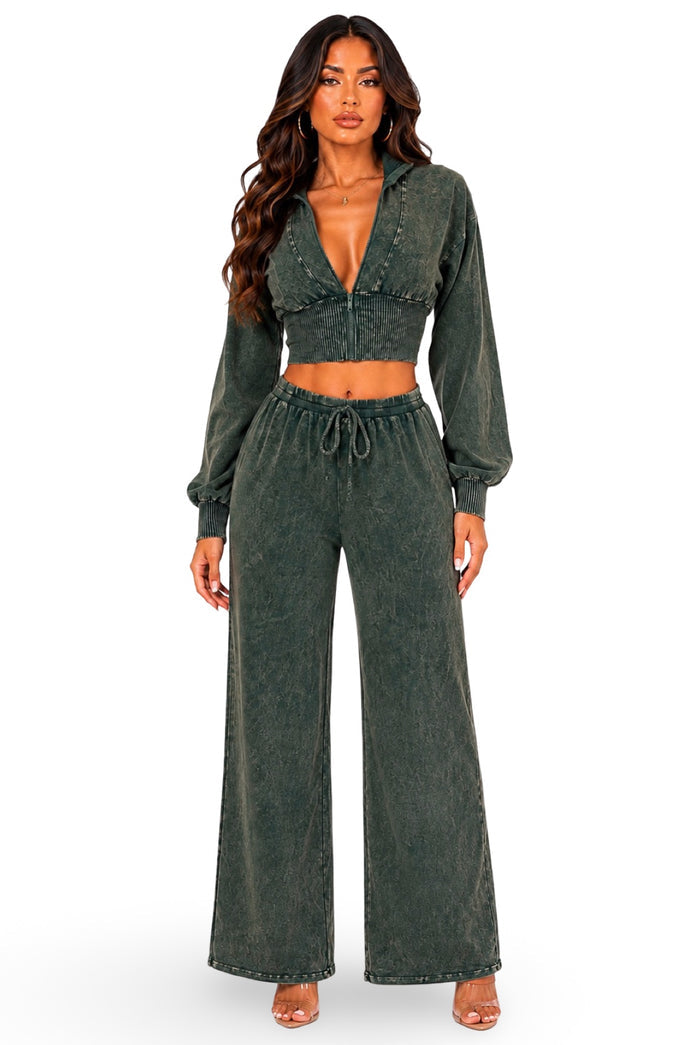 A woman modeling a matching two-piece lounge set in washed dark green. The set includes a long-sleeve cropped zip-front top with a deep V-neck and matching high-waisted wide-leg pants with a drawstring waist, shown against a plain white background.