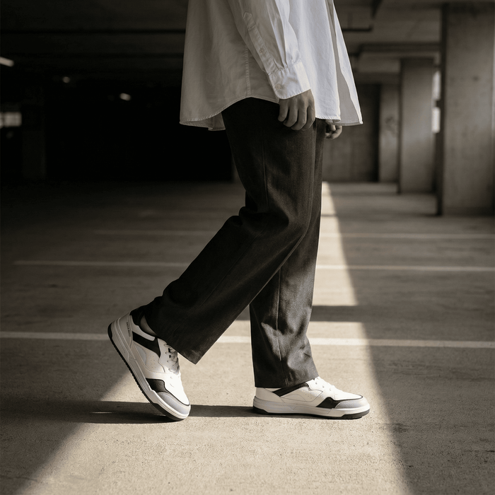 Person wearing bacca bucci  white sneakers with black stripes in a dimly lit parking garage.