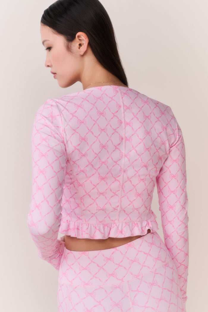 Woman wearing a pink bow patterned workout jacket and matching leggings against a plain background