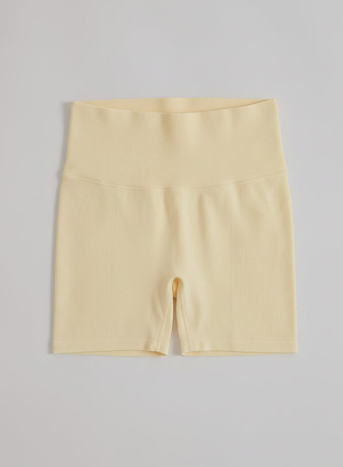 Keltaiset aim'n Shape Seamless Hotpants -shortsit korkealla ribbed-vyötäröllä tasokuvassa.