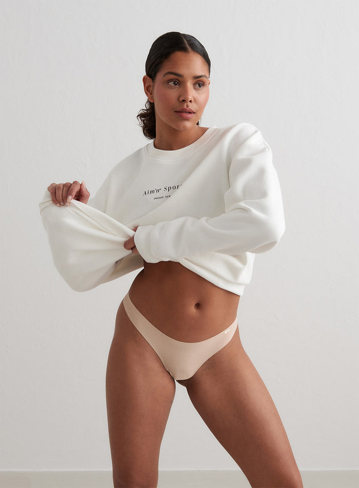 Malli yllään aim'n nude Beige Invisible Thong ja nostamassa ylös valkoista collegepaitaa