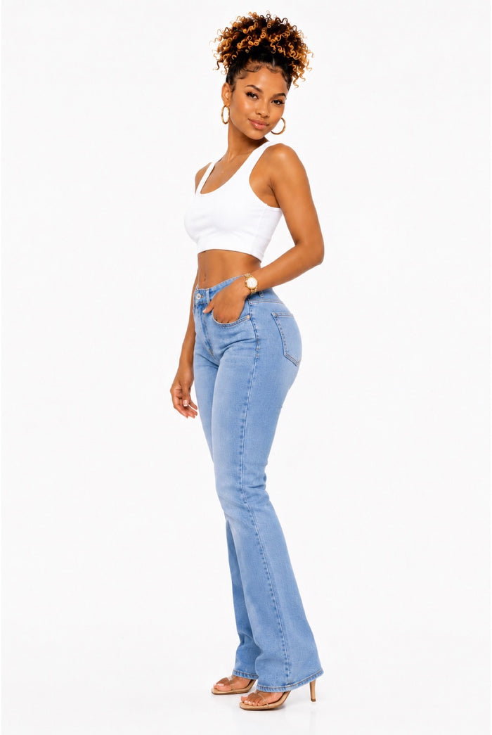 A woman modeling light-wash blue flare jeans with a white crop top, standing against a plain white studio background.
