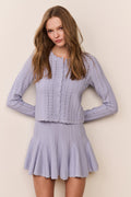 Woman wearing a blue knitted dress and cardigan set against a plain background