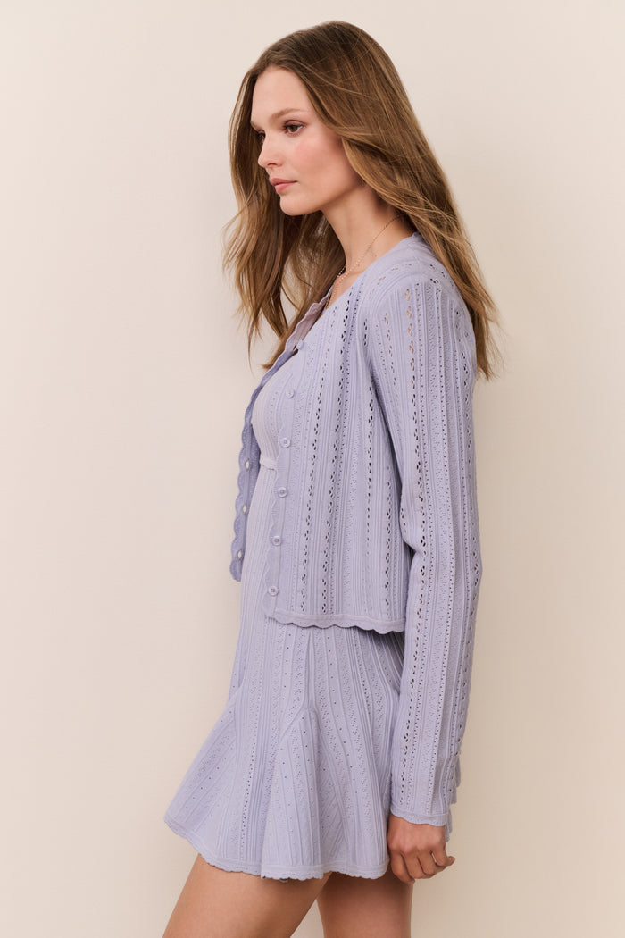Woman wearing a blue knitted dress and cardigan set against a plain background