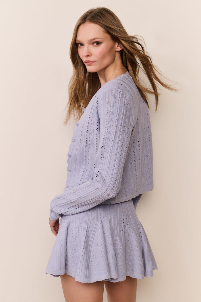 Woman wearing a blue knitted dress and cardigan set against a plain background