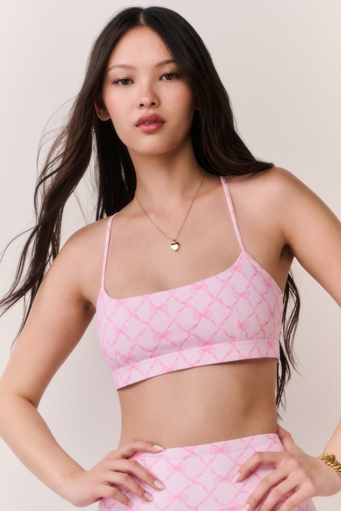 Woman wearing a pink patterned sports bra top and matching leggings against a plain background