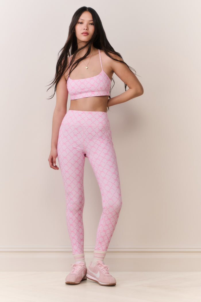 Woman wearing a pink patterned sports bra and matching legging on a plain background