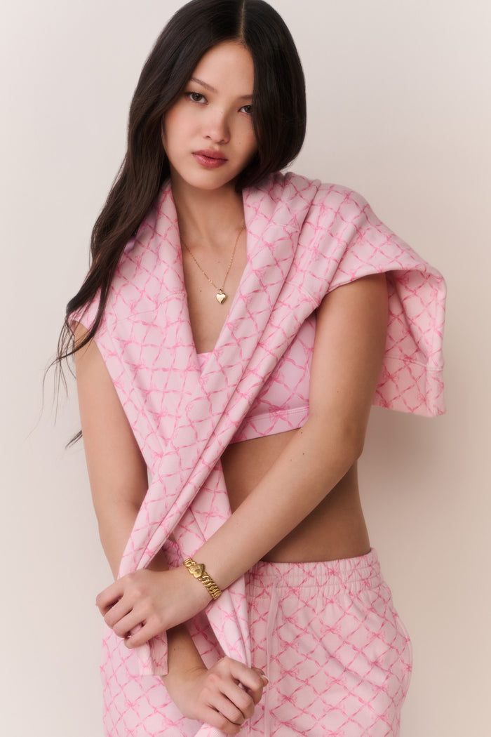 Person wearing a pink bow print jacket, sports bra, and matching sweatpants against a plain background
