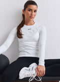 Mallilla on yllään valkoinen aim'n Soft Basic Long Sleeve -pitkähihainen, mustat trikoot ja valkoiset lenkkarit. Hän istuu alas kuntopallon viereen.