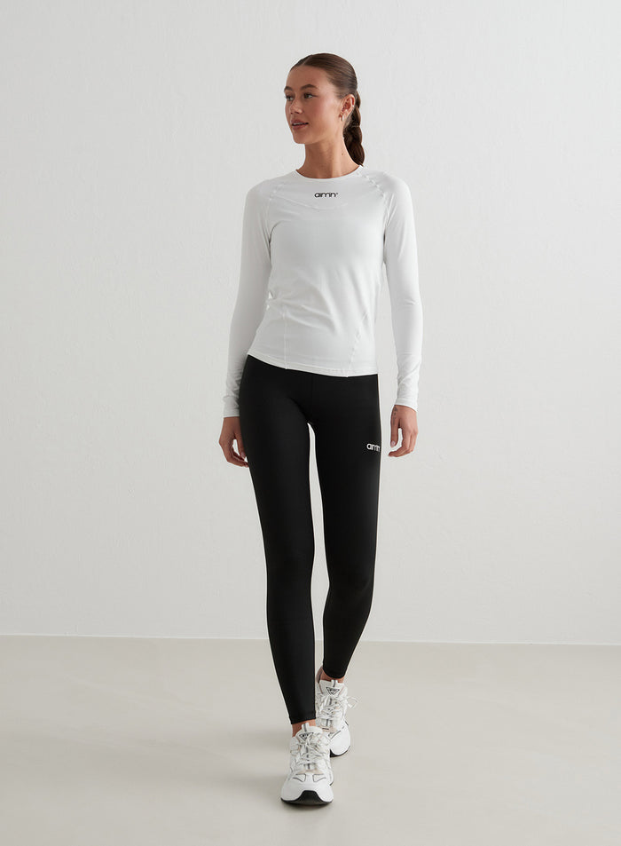 Valkoinen aim'n Soft Basic Long Sleeve raglanhihoilla ja koristesaumoilla sekä mustat leggingsit.